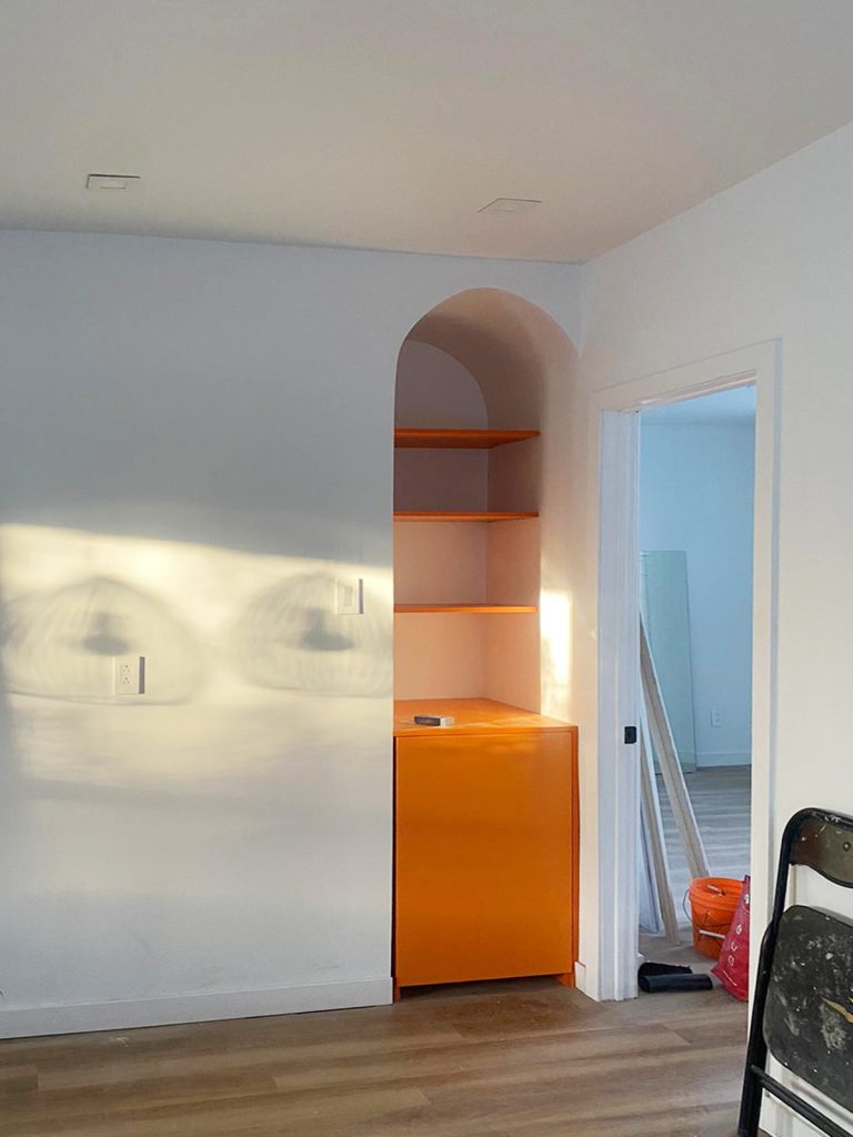 Bold orange alcove cabinet with matching open shelving in modern apartment