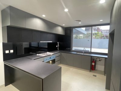 Sharjah Masaar Villa Custom Cabinetry & Garage Door Project 4 Modern U-shaped kitchen cabinets in grey and black with built-in appliances and large countertop space for a Sharjah Masaar villa.
