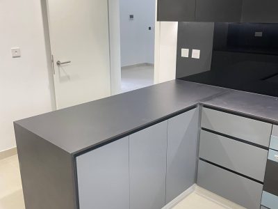 Sharjah Masaar Villa Custom Cabinetry & Garage Door Project 5 Close-up view of custom grey and black U-shaped kitchen cabinets with sleek countertop and handleless cabinet fronts.